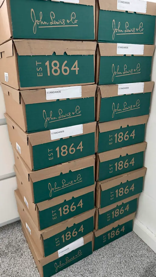 Two columns of green John Lewis delivery cartons stacked against a wall.