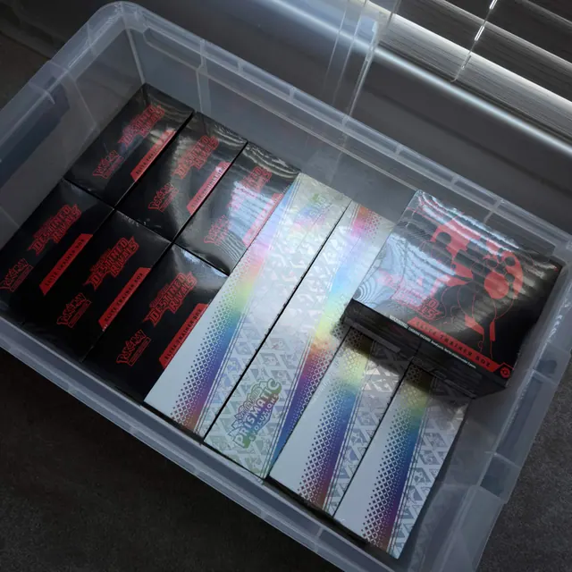 A clear storage container filled with Destined Rivals and Prismatic Evolutions boxes.