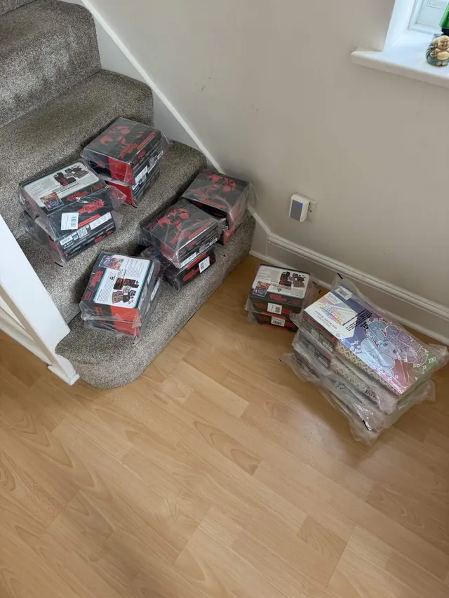 Dark Pokémon product boxes on a staircase beside wrapped collection boxes on the floor