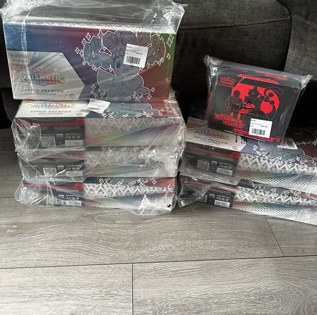 Destined Rivals and Prismatic Evolutions boxes stacked on a wooden floor.