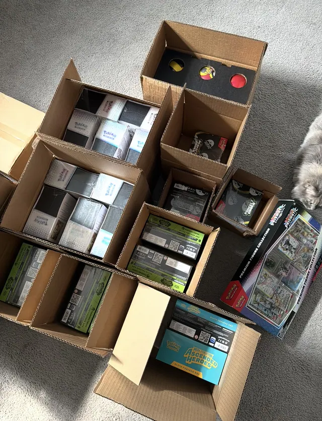 Open cartons filled with Pokémon Elite Trainer Boxes and assorted collections.