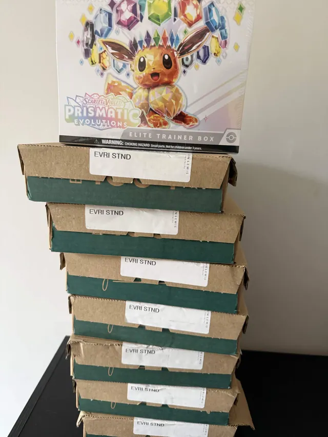 A Prismatic Evolutions Elite Trainer Box on top of stacked green delivery cartons