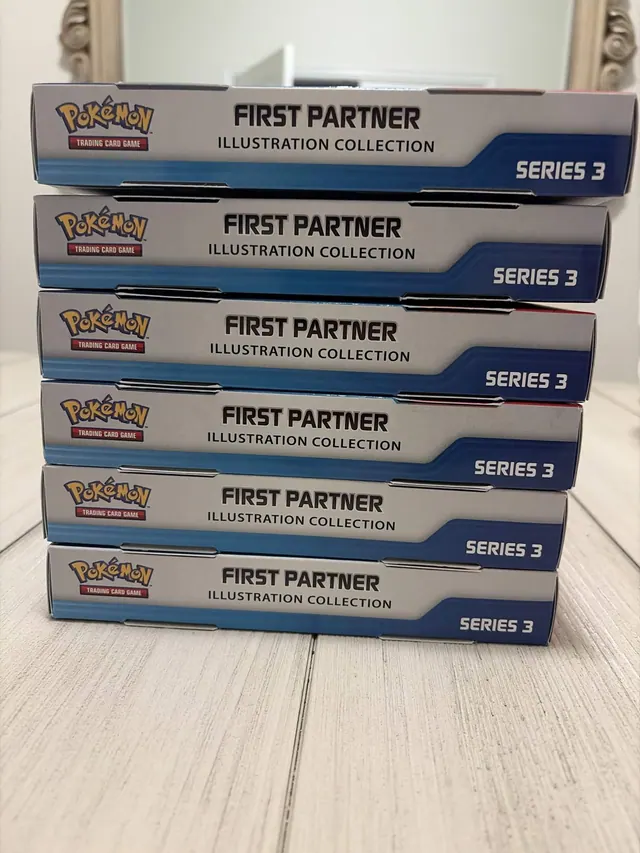 A stack of Pokémon First Partner Series 3 boxes on a wooden floor