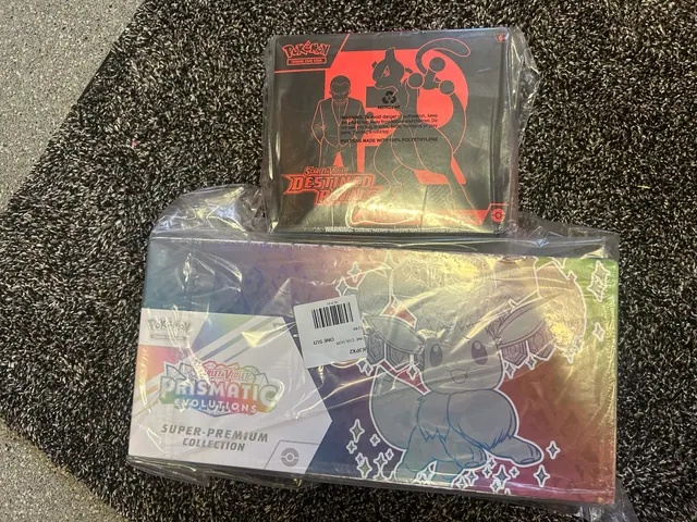 A red-and-black Pokémon box above a sealed Prismatic Evolutions collection box