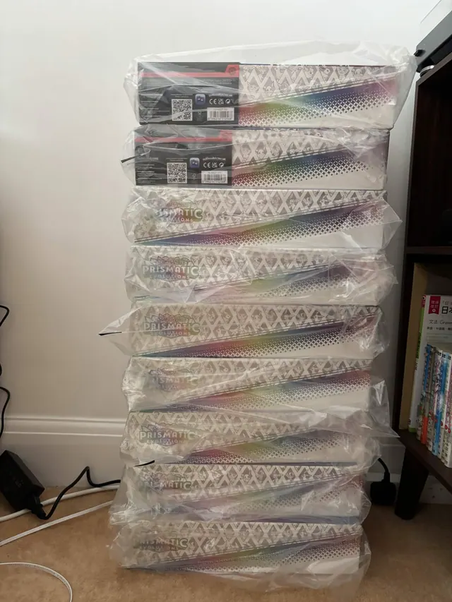 A tall stack of bubble-wrapped Pokémon collection boxes beside a cabinet.