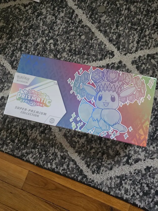 A Prismatic Evolutions Super-Premium Collection box on a patterned rug.
