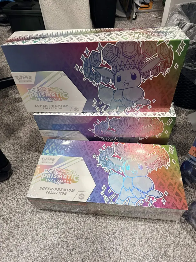 Two reflective Prismatic Evolutions collection boxes stacked on a carpet