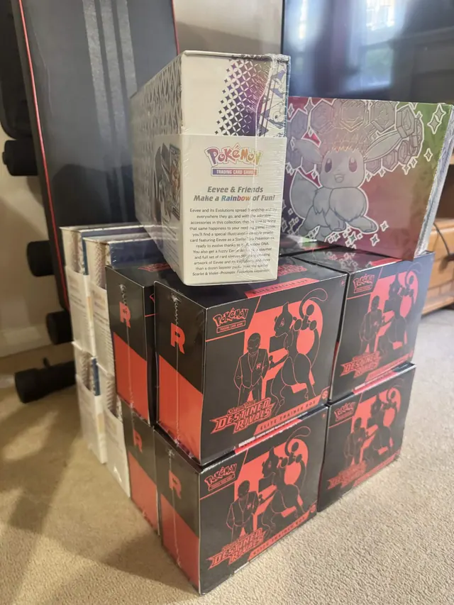 Pokémon 151 and Prismatic Evolutions boxes stacked above Destined Rivals boxes.
