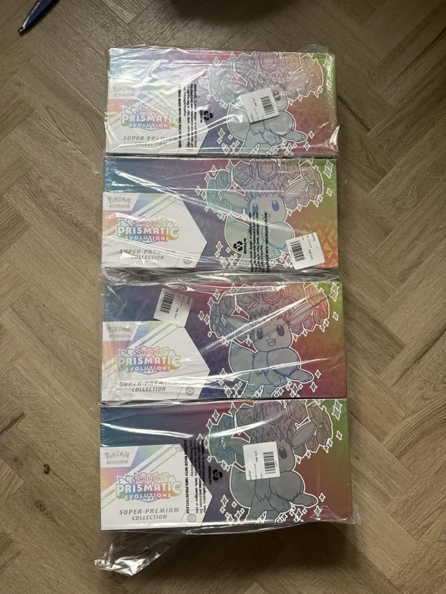 Four wrapped Prismatic Evolutions Super-Premium Collection boxes on a wooden floor.