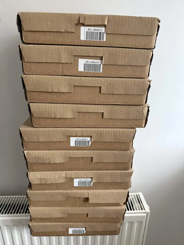 A tall stack of flat brown delivery cartons against a white wall.
