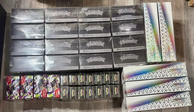 Sealed Pokémon boxes and booster packs arranged in rows on a wooden surface.
