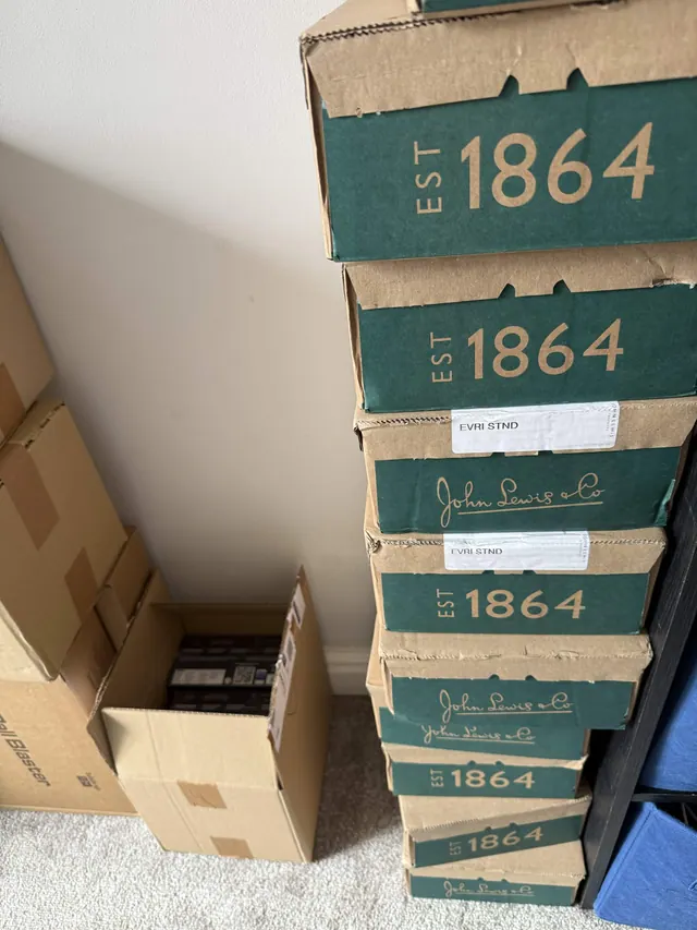 A tall stack of green John Lewis delivery boxes beside open cartons.