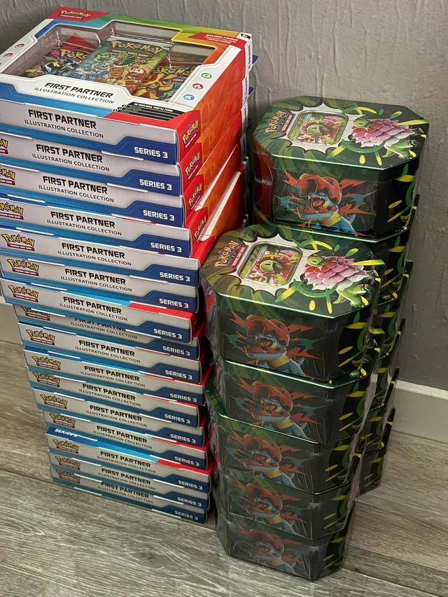 Tall stacks of rectangular Pokémon boxes beside green illustrated tins