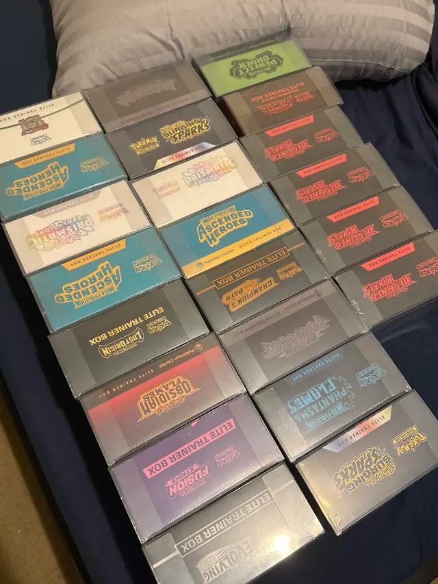 Rows of colorful Pokémon Elite Trainer Boxes laid out across a sofa