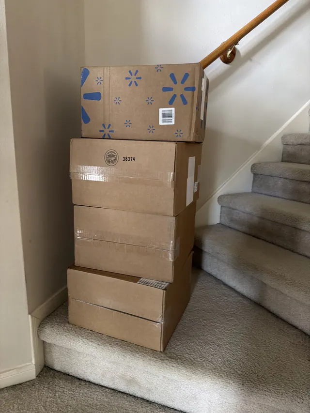 Large delivery cartons stacked beside a staircase, with a Walmart box on top.