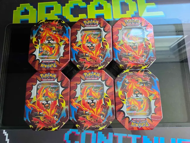 Six Charizard-themed Pokémon tins arranged on an arcade-themed surface.