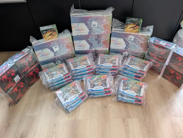 An assortment of sealed Pokémon collection boxes and card packs spread across a floor.
