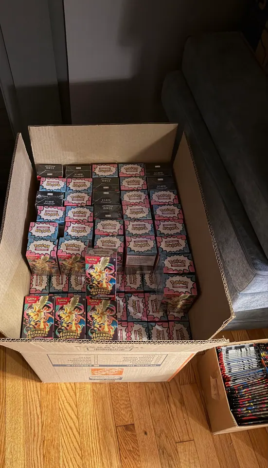 An open shipping carton filled with Pokémon tins and card products.