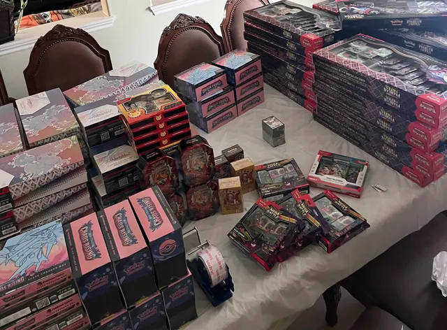 A dining table covered with Chaos Rising, Prismatic Evolutions and other Pokémon collections.